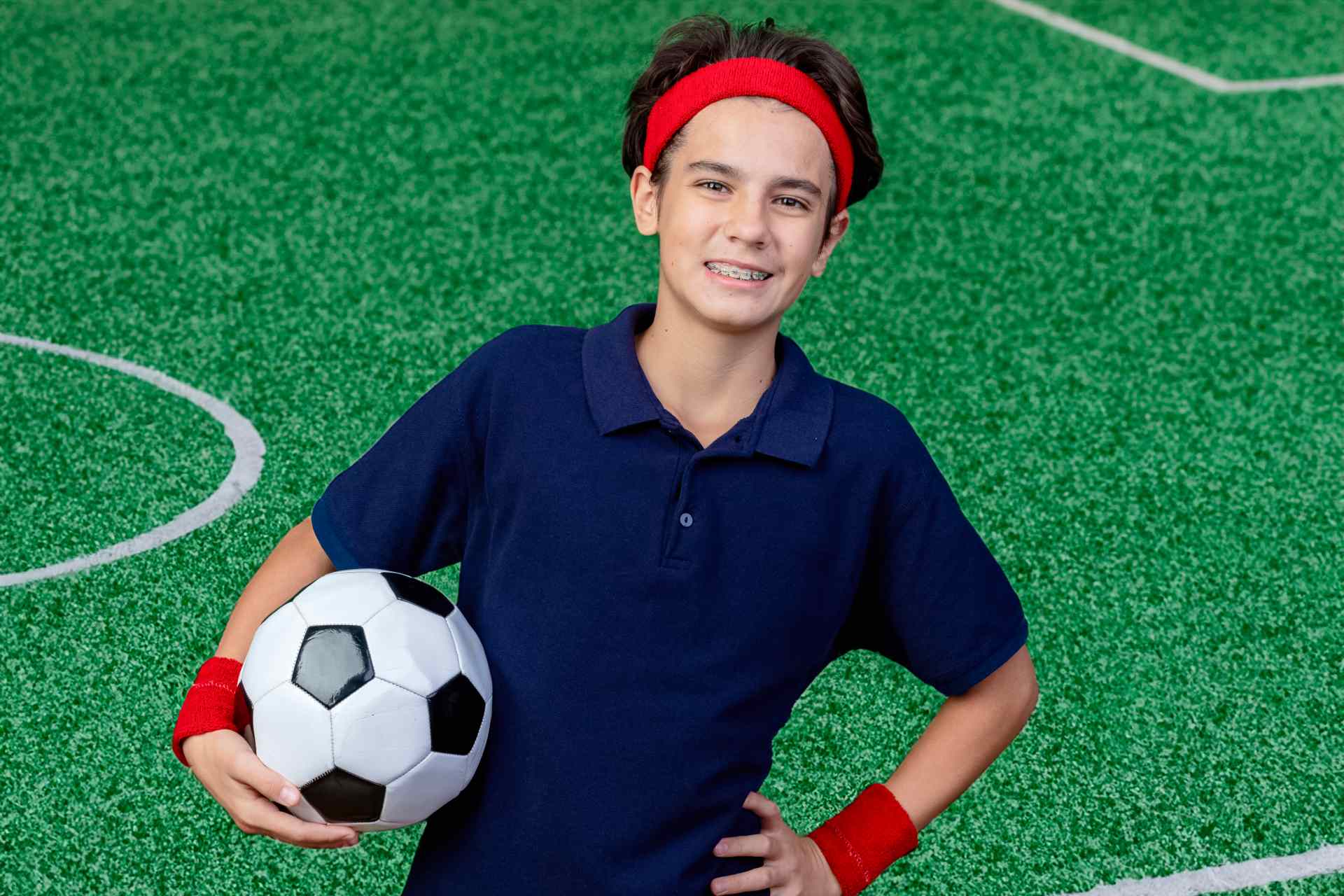 Teenager on a soccer field with braces holding a soccer ball.